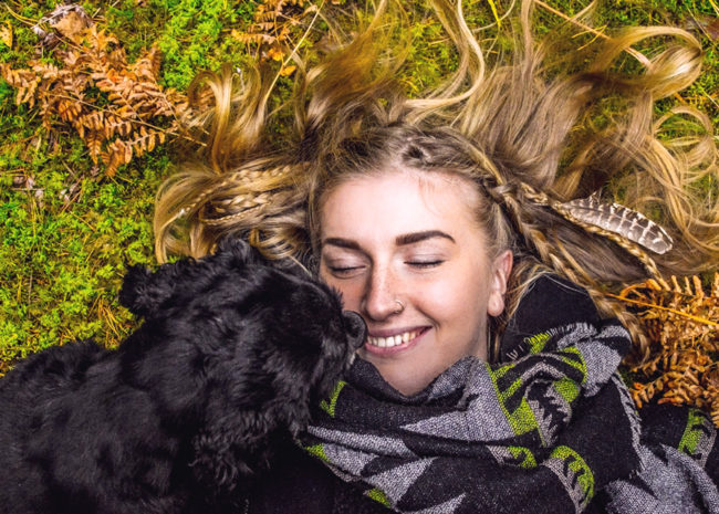 Uma mulher deitada na grama com um cachorro sorrindo.