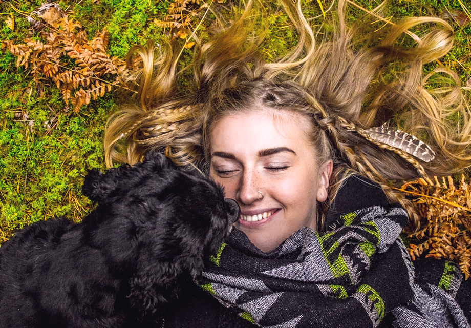 Uma mulher deitada na grama com um cachorro sorrindo.