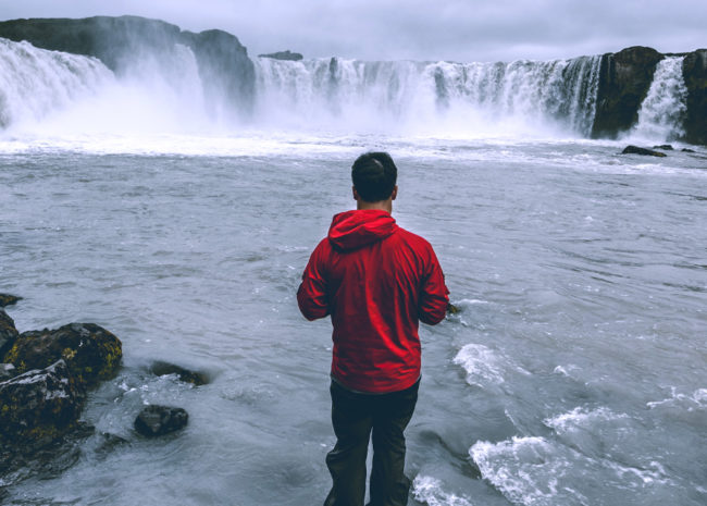 Um homem de costas olhando para uma cachoeira e refletindo sobre a sua vida.