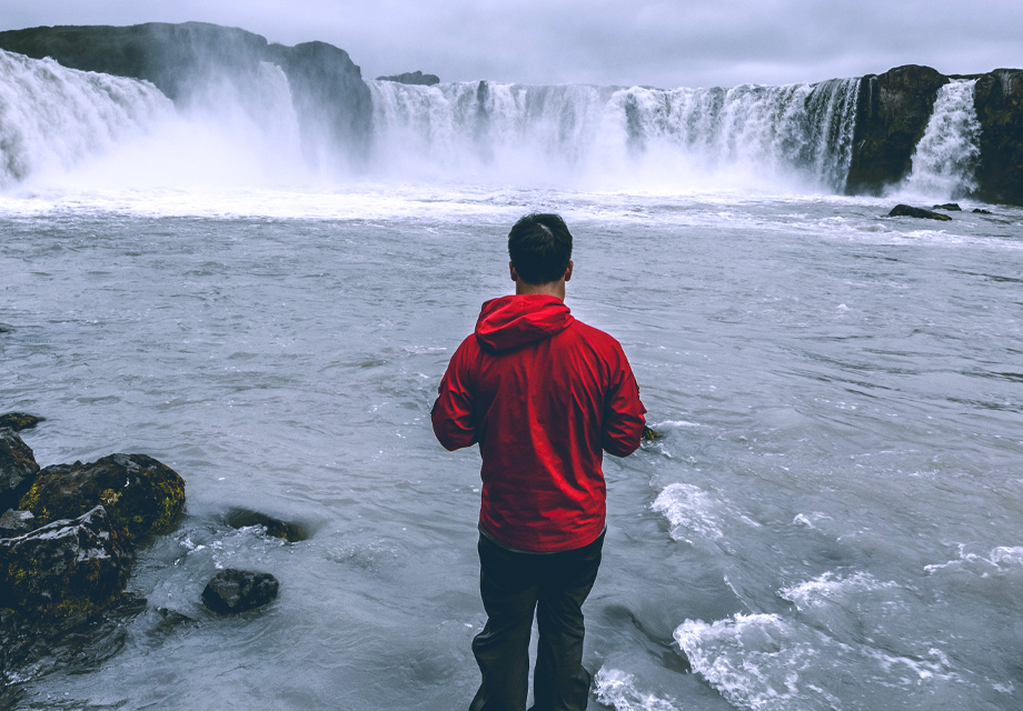 Um homem de costas olhando para uma cachoeira e refletindo sobre a sua vida.