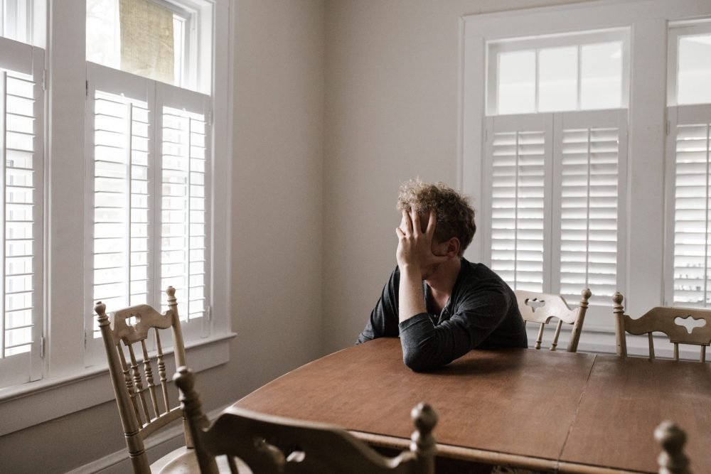 Um homem com a mão no rosto pois está cansado e não aguenta mais pensar em seu passado.