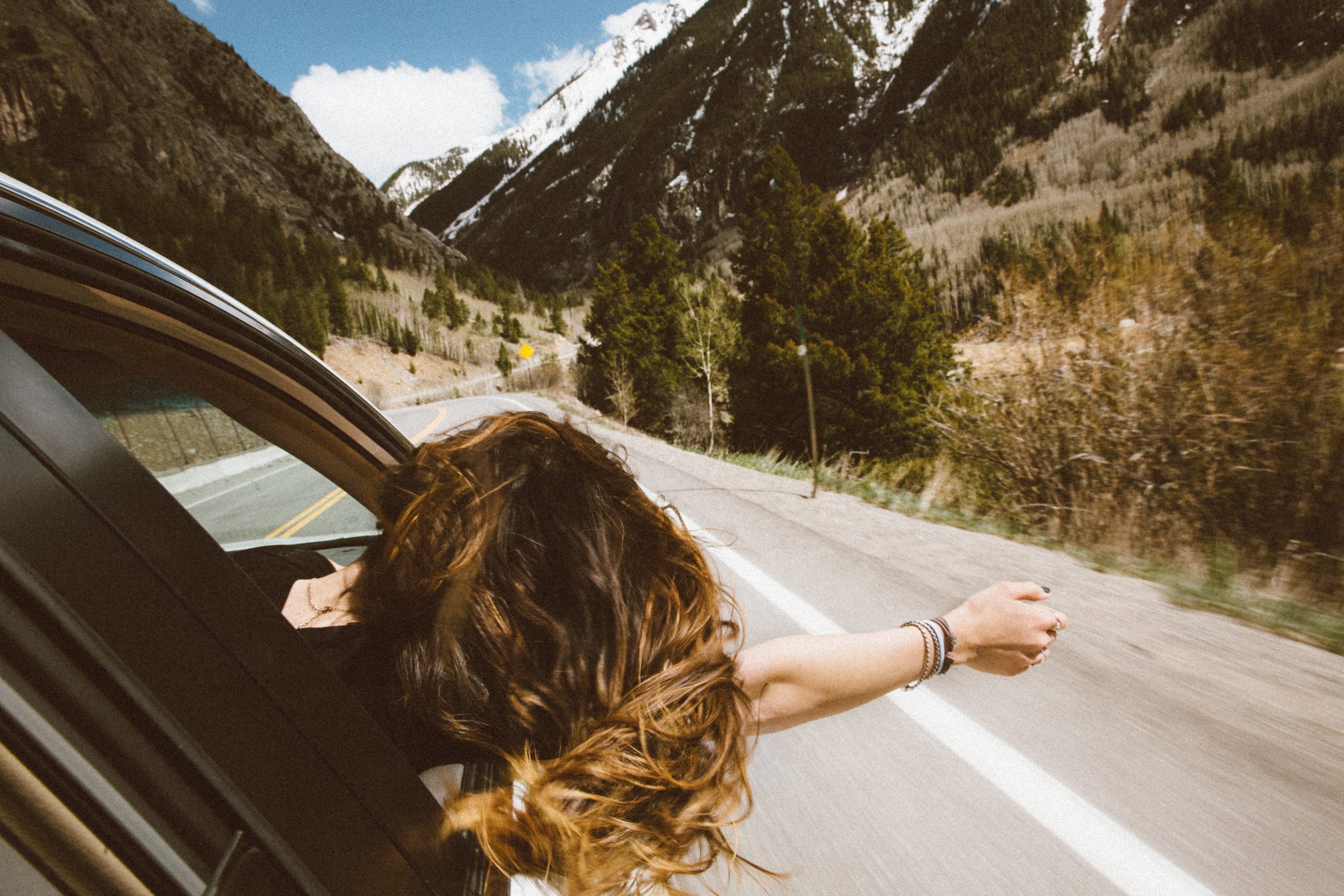 Uma mulher com a cabeça e o braço para fora do carro, ela está se sentindo livre de incertezas em sua vida.