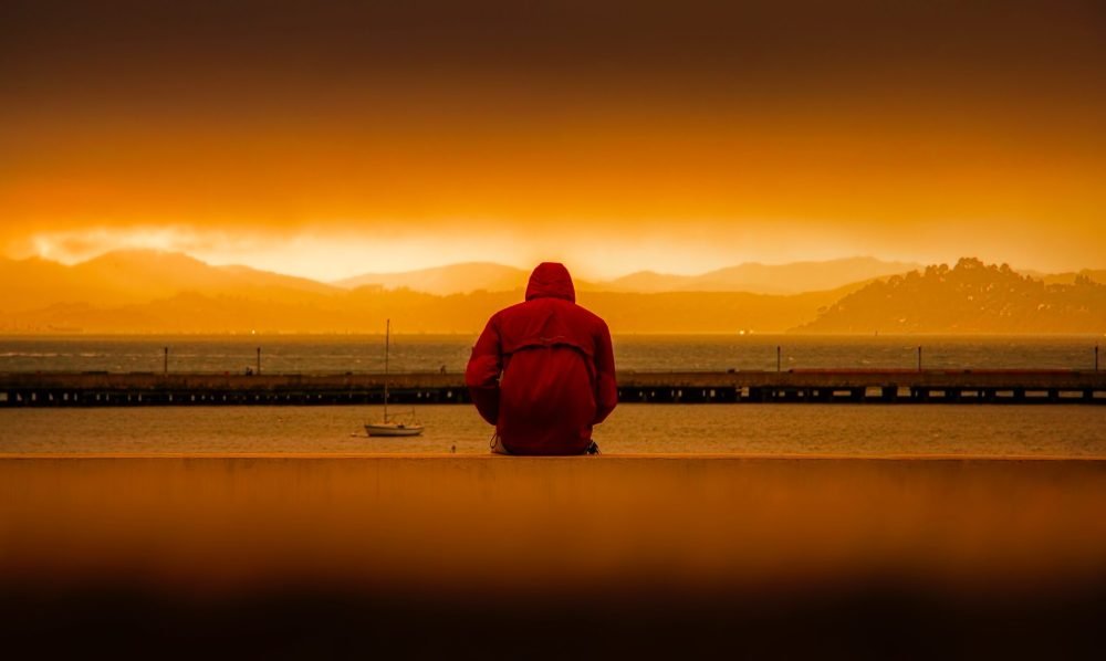 Um homem sentado longe, pois está com depressão. Ele está confuso, pois não sabe quais são os níveis da depressão.