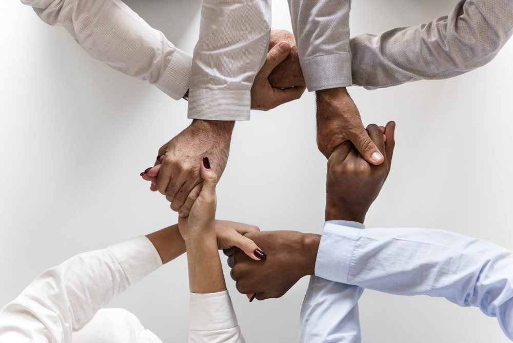 alt="Imagem de pessoas diversas com as mãos dadas."